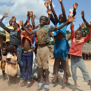 Children in a village in Ghana cheering and waving their arms in celebration. 